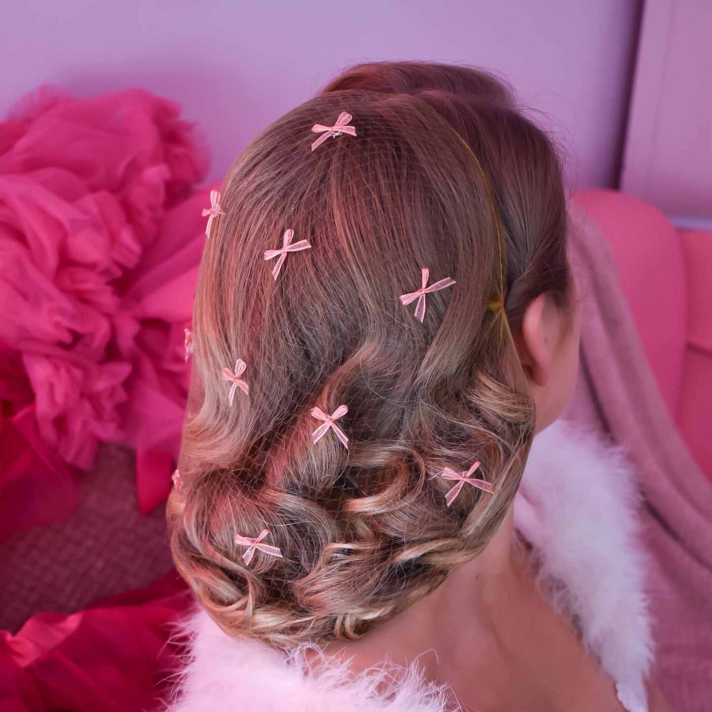 Back view of a person with styled hair featuring pink hair clips against a pink background