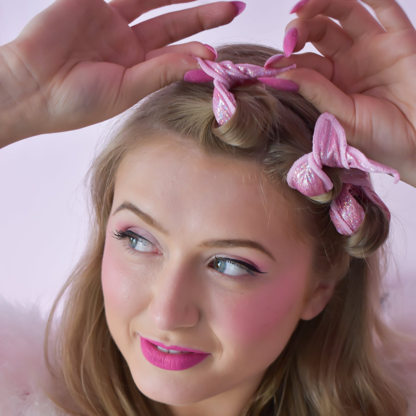 Woman with pink hair rollers in her hair against a pink background