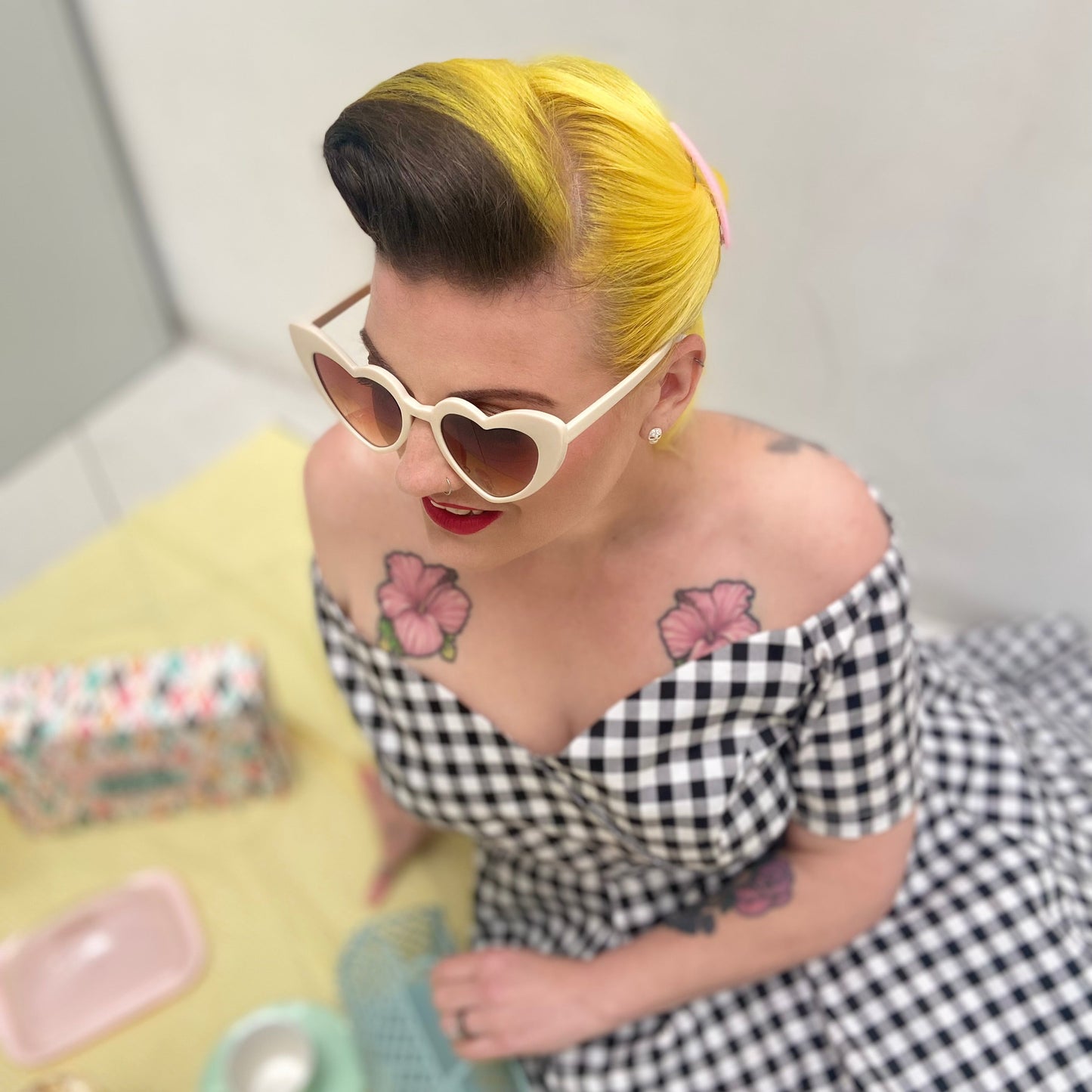Person with yellow hair and tattoos wearing a checkered dress, sitting at a table.