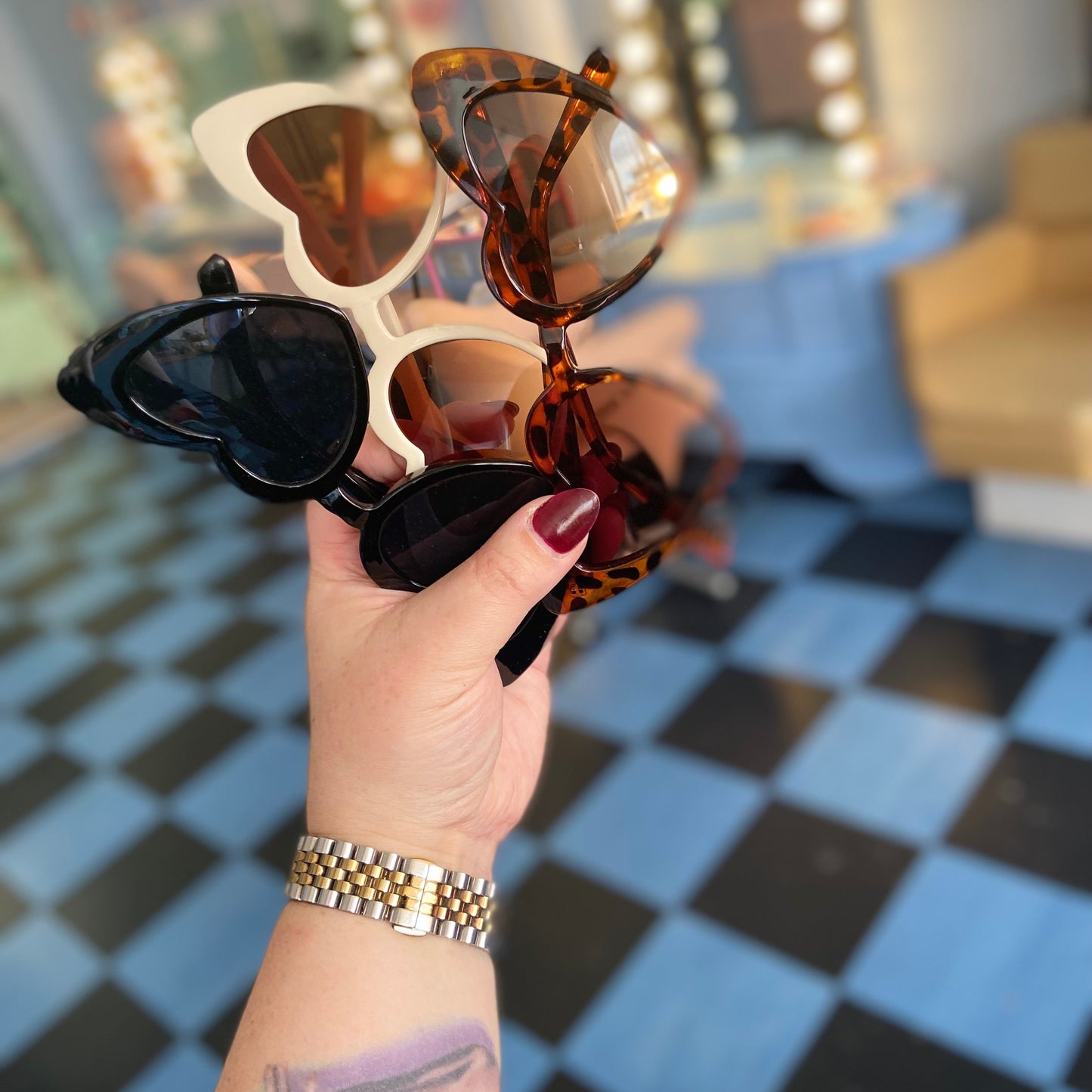 Hand holding three pairs of sunglasses with a blurred background
