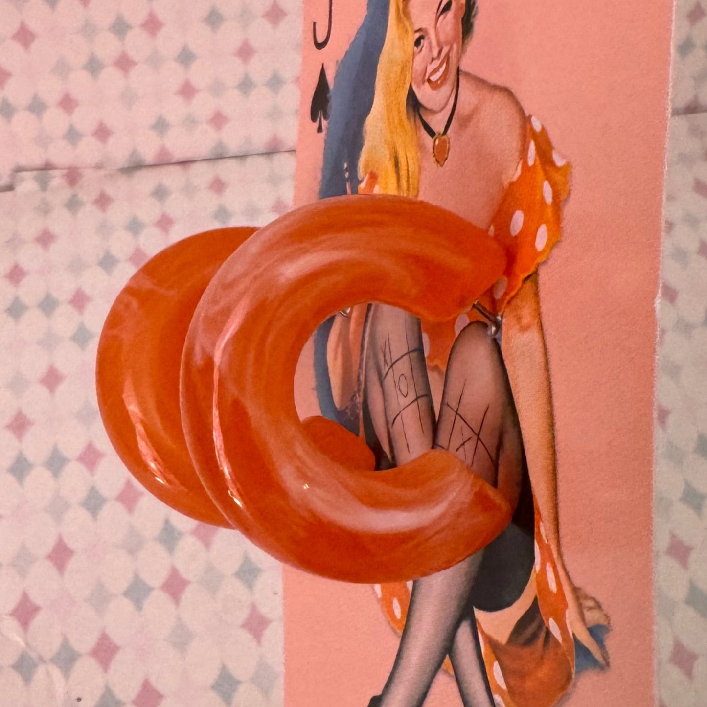 Orange ring held over a card with a design on a patterned surface