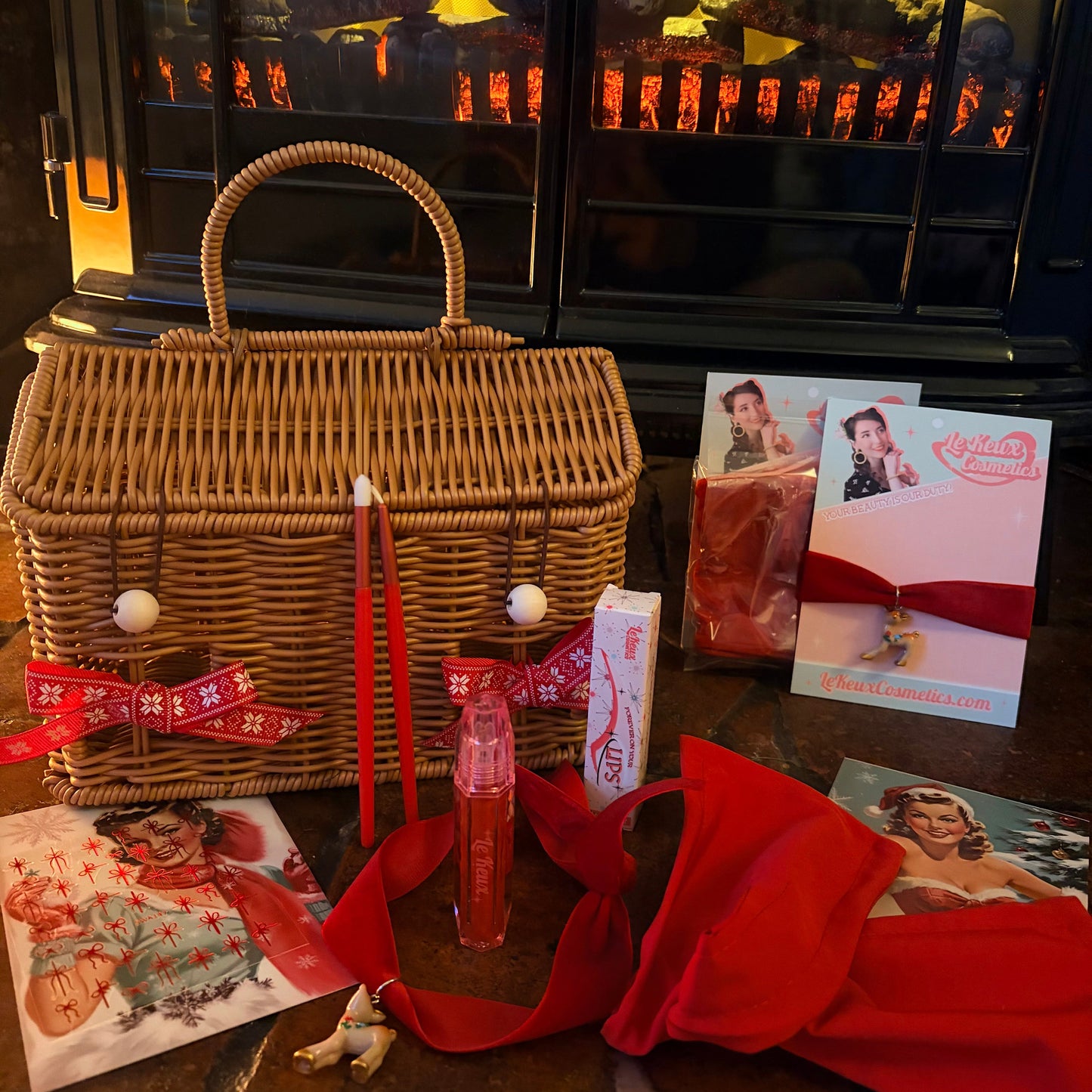 Wicker picnic basket with red ribbon and cards on a table in front of a lit fireplace.
