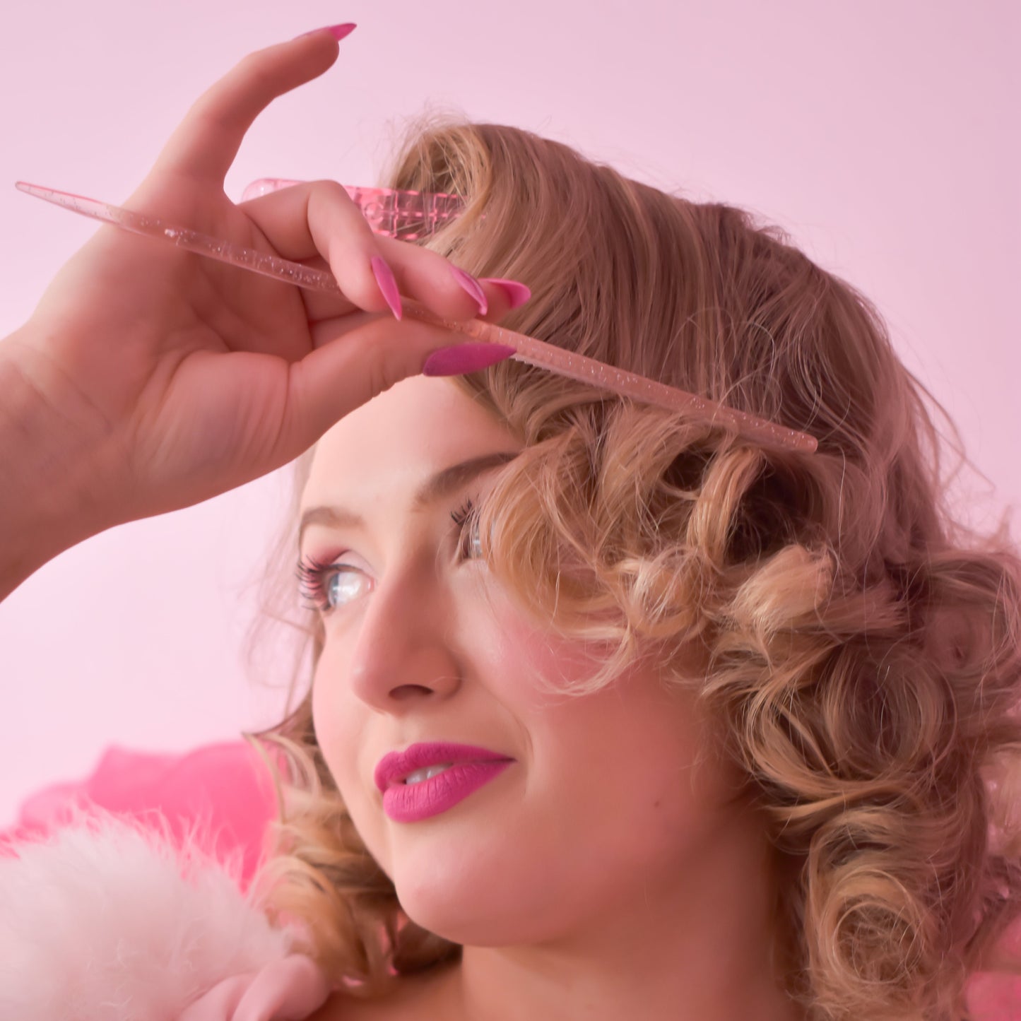 Woman with styled hair and pink makeup against a pink background