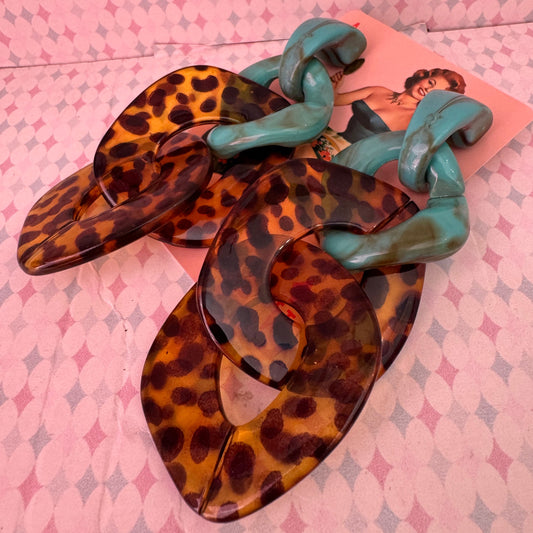 Pair of leopard print earrings with green straps on a pink patterned surface
