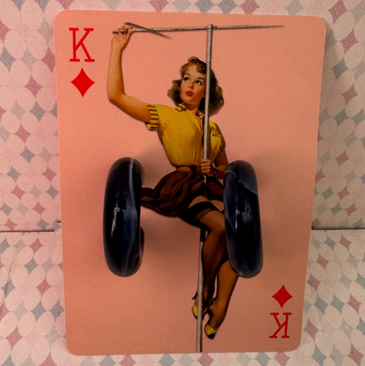 Playing card with a vintage-style illustration of a woman on a unicycle, on a patterned surface.