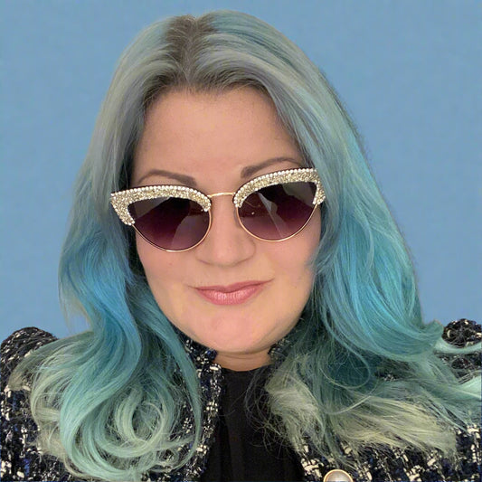 Person with blue hair wearing large sunglasses and a patterned jacket.